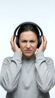 Young woman wearing headphones with annoyed expression covering ears against loud noise isolated on white background for audio and sound concepts.
