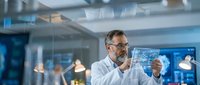 Middle-aged Caucasian male scientist in white lab coat examining transparent digital tablet with data visualization in modern research laboratory.