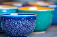 Colorful ceramic bowls with dotted pattern, navy blue and turquoise pottery in soft focus. Handcrafted artisanal tableware showcases traditional decorative technique.