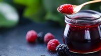 Fresh berry jam in glass jar with wooden spoon and mixed berries on dark surface. Homemade preserve for breakfast, baking and culinary projects.