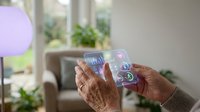 Senior woman using transparent smartphone with holographic interface displaying digital icons in modern home interior for futuristic technology concepts.
