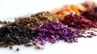 Aromatic loose tea leaves in vibrant purple, black and orange colors arranged on white surface, showing texture and natural organic ingredients for brewing.
