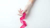 Gloved hand holding a pink ribbon on white background, symbolizing breast cancer awareness, health support, and medical solidarity.