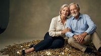Happy senior Caucasian couple sitting together on couch smiling warmly at camera in elegant home setting for lifestyle and relationship concepts.