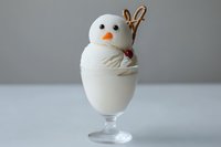 Cute snowman dessert made from white ice cream or mousse in glass with pretzel stick arms and orange carrot nose for winter holiday treats.