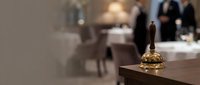 Elegant hotel reception desk with golden service bell in luxury lobby interior with blurred guests and staff in background for hospitality industry.