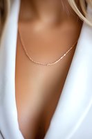 Delicate rose gold chain necklace on feminine neckline with soft white fabric draping, creating elegant minimalist jewelry styling for fashion and accessory marketing.