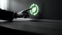 Hand holding glowing green recycling symbol on dark surface, representing sustainability, environmental responsibility, and eco-friendly business practices.