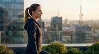 Young professional woman in athletic wear standing on urban rooftop terrace during golden hour sunset with city skyline and construction cranes in background.