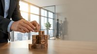 Businessman building wooden blocks with customer service icons on office desk representing quality management and business growth strategy.