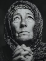 Dramatic black and white portrait of elderly Caucasian woman with headscarf gazing upward, weathered face showing life experience, hands clasped in prayer or contemplation.