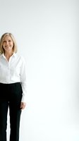 Confident mature blonde businesswoman in white shirt and black pants smiling against clean white background for corporate presentations.
