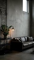 Industrial loft interior with gray leather sofa, potted plant, pendant lamp, and exposed brick wall with large window for modern home design and commercial spaces.