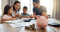 Happy Hispanic family with two children learning financial planning and budgeting skills together at home with piggy bank and coins on wooden table.