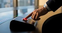 Businessman hand pressing red emergency button on desk in modern office environment for crisis management and urgent decision making concepts.