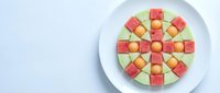 Colorful fruit cubes arranged in geometric pattern on white plate. Fresh melon and watermelon pieces create vibrant mosaic design for healthy eating concepts.