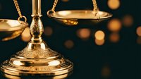 Golden scales of justice with ornate details against dark background with warm bokeh lights for legal and judicial concepts.