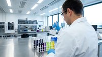 Male scientist in white lab coat conducting research with test tubes in modern laboratory facility with advanced equipment and bright lighting.