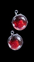 Red liquid spheres with tiny bubbles floating against black background, macro photography showing surface tension and light reflection in water drops.