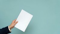 Hand holding blank white paper sheet against turquoise background for mockup, branding, advertising, and presentation purposes.