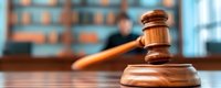 Wooden judge gavel on court desk with blurred courtroom background showing legal professional. Justice and law enforcement concept for legal presentations.