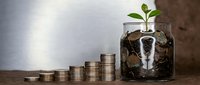 Young green plant growing from coins in glass jar with stacked money representing financial growth, investment success and wealth building concept.