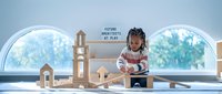 Young African American girl architect playing with wooden building blocks creating structures by large arched windows in bright modern room.