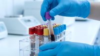 Young scientist or laboratory technician with light skin tone wearing blue protective gloves handling colorful blood sample tubes in a medical research or diagnostic testing facility for healthcare and clinical analysis.