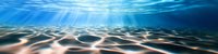 Underwater sun rays penetrate crystal clear ocean water creating mesmerizing light patterns on sandy seabed, panoramic view of tranquil marine landscape.