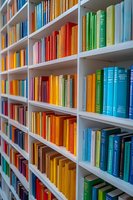 Colorful books arranged by spectrum colors on white library shelves creating rainbow effect, organized collection for education, reading and literature background.