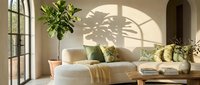 Bright Scandinavian living room with cream sofa, green botanical pillows, fiddle leaf fig tree, and dramatic leaf shadow on warm beige wall.