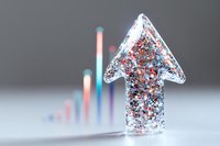 Glittery arrow shape filled with red and silver sparkles pointing upward against blurred colorful chart background, representing business growth and success trends.