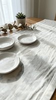 Minimalist dining table setup with white ceramic bowls on neutral linen tablecloth, succulent plant and eucalyptus branches for home decor and interior styling.