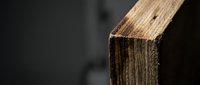 Weathered wooden beam edge showing natural grain texture and aging patterns against dark background for construction and carpentry projects.