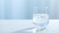 Glass of cold water with ice cubes on white surface against blurred blue background, suitable for beverage, health, wellness and refreshment concepts.