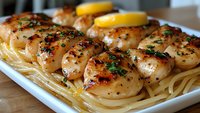Pan-seared scallops with herbs and lemon slices served over linguine pasta on white plate. Gourmet seafood dinner with golden-brown seared shellfish and garnish.