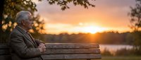 Elderly Caucasian man sitting alone on a park bench at sunset, gazing at the horizon with a contemplative expression near a tranquil lake.
