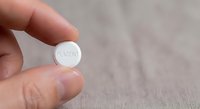 Hand holding white round pill tablet with PLACEBO text on wooden surface for medical research and pharmaceutical testing concepts.