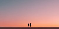 Two silhouetted figures walking together on horizon against stunning pink and orange sunset sky creating romantic peaceful scene for travel and relationship concepts.