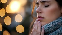 Young Caucasian woman in warm scarf praying with closed eyes against blurred golden bokeh lights background, side view portrait showing peace and spirituality.