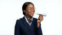 Professional African American female pilot in navy uniform holding paper airplane with joyful expression on white background isolated for design.