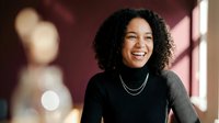 Happy young African American woman with curly hair smiling warmly in modern office setting with natural lighting and bokeh background.