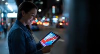 Young woman using tablet computer at night in urban city street with bokeh lights background for digital technology and mobile connectivity concepts.