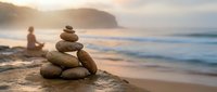 Balanced stone cairn on beach at sunset with person meditating in background. Zen meditation concept for wellness and mindfulness practices.