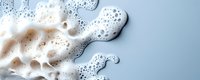 White soap foam with bubbles on light blue background, abstract cleaning texture with copy space for text, macro photography of washing detergent suds.