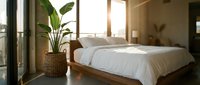 Serene bedroom with wooden bed, white linens, potted plant in wicker basket, and natural sunlight from large windows for home decor and interior design projects.