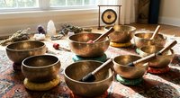 Tibetan singing bowls meditation set with wooden mallets arranged on ornate carpet near window for sound healing therapy and mindfulness practice.