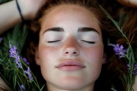 Young Caucasian woman with freckles lying peacefully with closed eyes surrounded by fresh lavender flowers for natural skincare and wellness concepts.