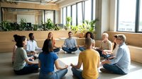 Diverse group of people sitting in circle practicing meditation and mindfulness in modern office space with natural light and plants.