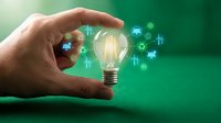 Hand holding glowing light bulb with renewable energy icons on green background representing sustainable innovation and eco-friendly technology solutions.
